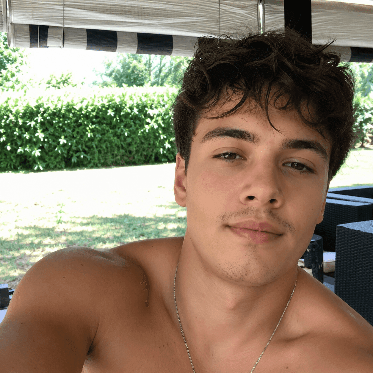 Before jawline filter: shirtless man with a necklace on his porch with a slightly weak jawline